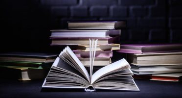 open-book-in-front-of-stack-of-books-on-dark-surfa-2021-08-30-19-34-19-utc